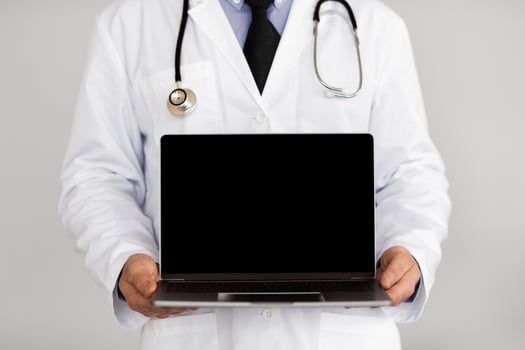 Adult male doctor holding laptop computer with black blank screen mock up, isolated over white studio background photo