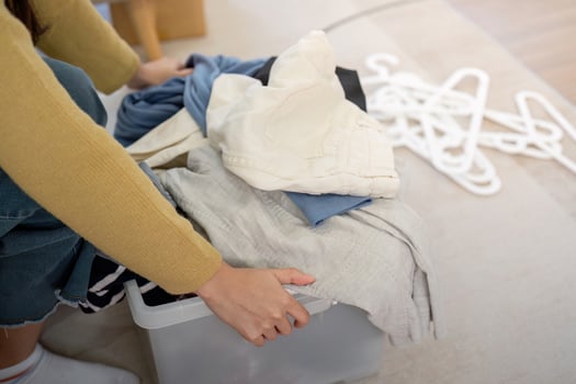 Close-up of a woman hands organizing clothes in a transparent donation box, preparing for charity photo