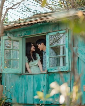 Couple gazing lovingly from rustic teal cabin window, spring blossoms in background romantic relationship image photo