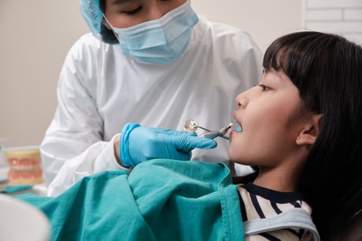 Asian female pediatric dentist examines a Thai girl's caries teeth in dental clinic, well-being mouth oral hygiene, and professional orthodontic healthcare work in a kid hospital. photo