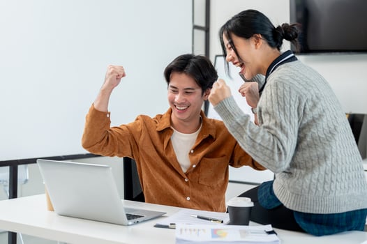 Two cheerful Asian businesspeople raise their triumph fists while looking at a laptop screen. photo