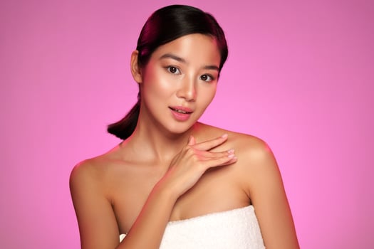 Woman with natural makeup poses gracefully against a pink background while displaying skincare routine photo