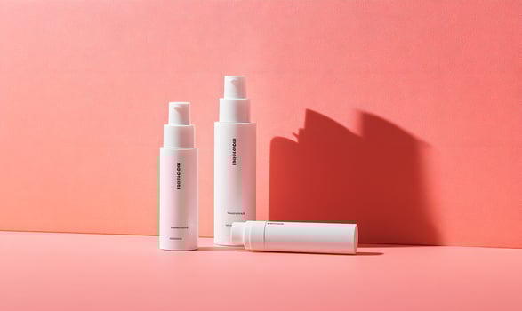 Three White Skincare Bottles on Coral Background photo