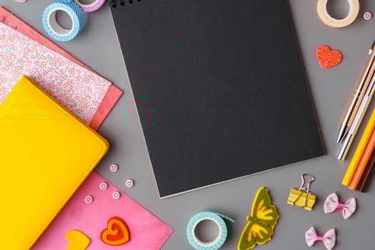 Crafting supplies arranged on a gray surface with a blank notebook, scissors, washi tape, and colorful embellishments photo