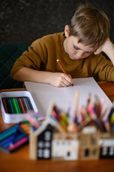 A boy sits with colored pencils, gazing at the paper, deciding what to draw. photo