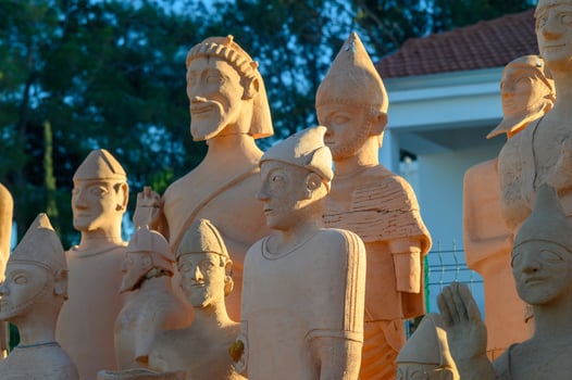 Clay sculptures of ancient figures stand proudly under a warm sunset in an outdoor exhibition space photo