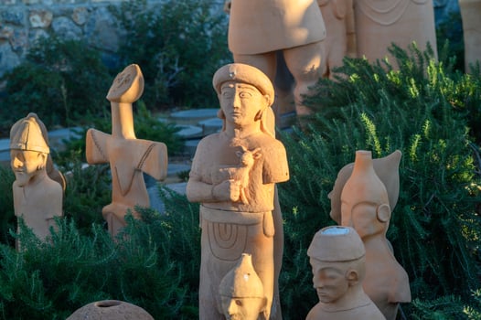 Ancient terracotta figures standing among green foliage in a serene outdoor setting during golden hour photo