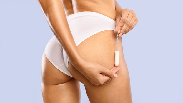Closeup cropped view of unrecognizable young woman in white panties holding absorbent tampon neak buttocks, rear back view, isolated on blue studio background, banner. Menstrual Cycle photo