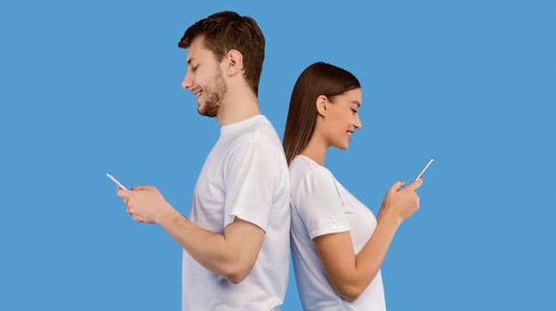 Portrait of young couple standing back to each other and looking at their cell phones, banner, copyspace photo