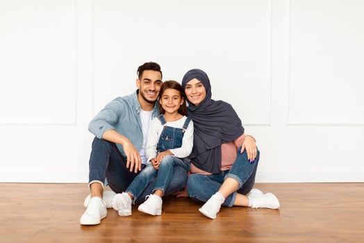 Happy Loving Family. Portrait of smiling muslim people sitting on the floor near wall in new apartment. Cheerful man, woman in hijab and little girl posing looking at camera, celebrating moving day photo