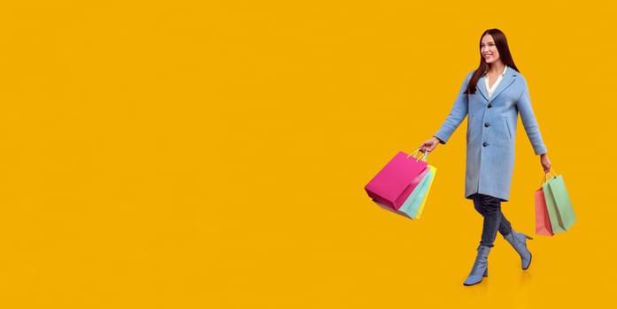 Time For Shopping. Cheerful young woman wearing coat and boots walking with bags from mall, copy space photo