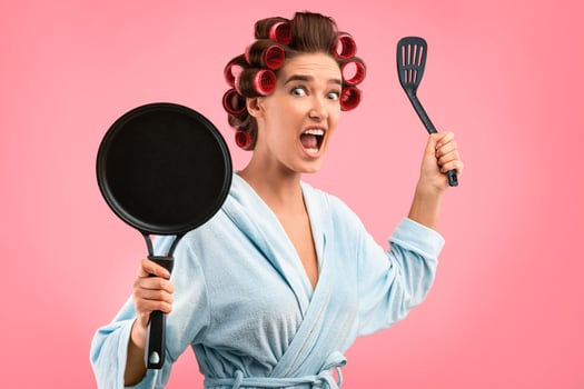 Crazy Housewife. Girl Holding Frying Pan Threatening And Shouting Looking At Camera Posing In Studio Over Yellow Background. photo