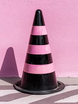 Pink and black traffic cone against pink wall photo
