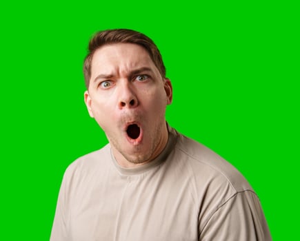 A surprised man stands in front of a bright green screen, expressing shock with his mouth open photo