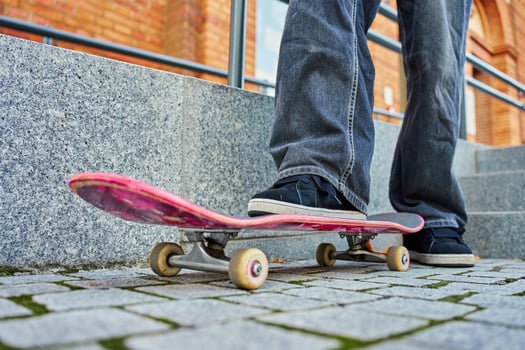 Skateboarder riding on pink skateboard. Close-up of teenager feet wearing jeans and black sneakers skateboarding at street stairs. Leisure activity and extreme sport concept photo