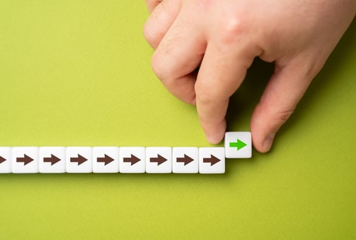 A hand makes a path out of blocks with arrows. The concept of moving forward and continuing progress. Strategic planning, forward momentum, and the continual pursuit of growth and improvement photo