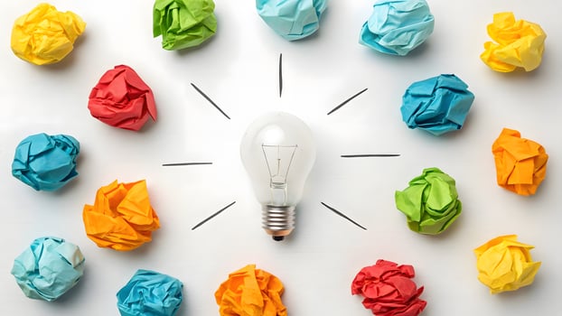Light bulb surrounded by colorful crumpled paper balls on white background. photo