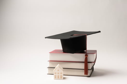 Graduation Cap Resting on Stacked Books With a Small House Figurine Beside It in a Minimalistic Setup photo