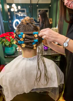 a young girl is getting her hair curled with curlers by a hairdresser. the client is sitting in a chair in a beauty salon. her hair is being styled. her hair will be curly and wavy photo