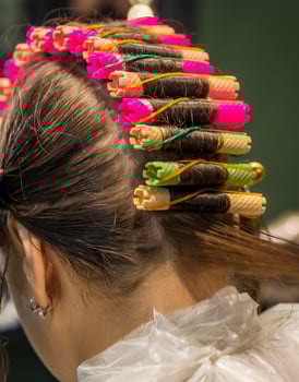 In a beauty salon, a girl is getting her hair curled. The curlers are shown in close-up. The girl is getting wavy curly hair. The hairdresser in the salon is curling the last strand of hair. photo