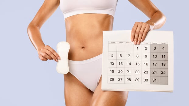 Period And Female Hygiene Protection. Closeup cropped view of unrecognizable woman in white underwear holding menstrual pad and paper calendar isolated on blue studio background, banner photo