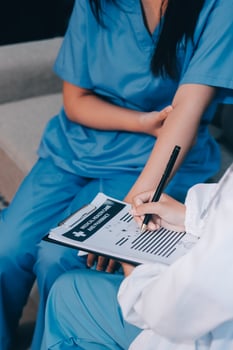A nurse is writing on a clipboard while another woman sits on a couch photo