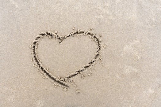 Symbol of heart written by hand on sand of beach with copy space photo
