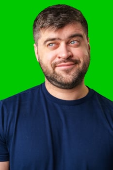 A young man smiles playfully against a bright green backdrop, showcasing a cheerful expression photo