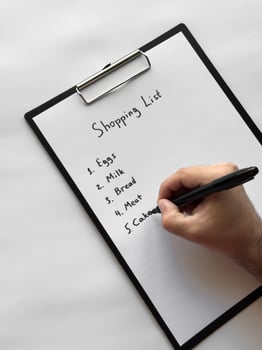 Hand writing shopping list on clipboard with eggs, milk, bread, meat, cakes items photo
