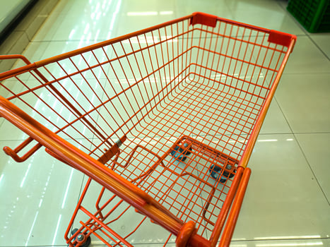 An empty orange shopping cart with a wireframe design is seen in a brightly lit supermarket aisle, ready for use photo