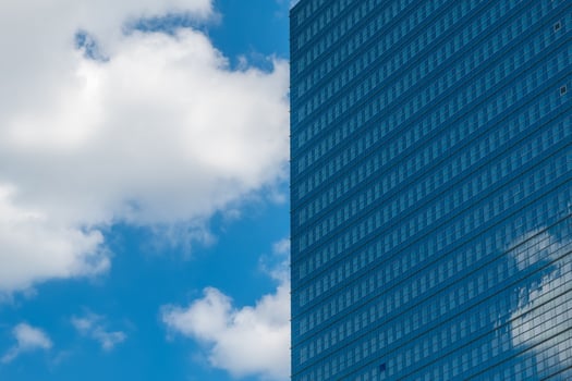 Modern glass building reflects clouds in a clear blue sky during a sunny day in an urban environment photo