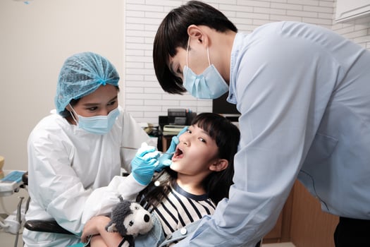Female pediatric dentist examines Asian girl's teeth in dental clinic and takes care and encourages of father, mouth oral hygiene, and professional healthcare work in a kid hospital. photo