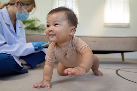 Happy baby crawling on the floor while pediatrician observes with a caring smile photo