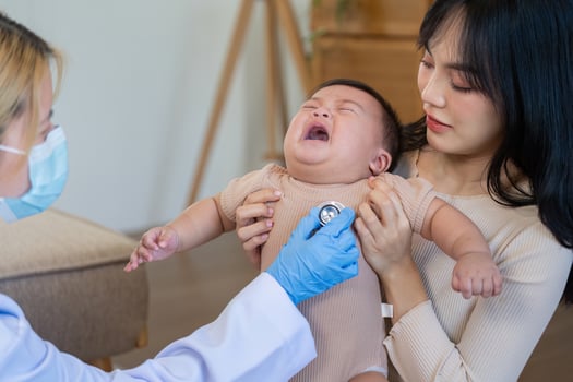 Concerned doctor examining crying baby with mother present during pediatric check-up photo