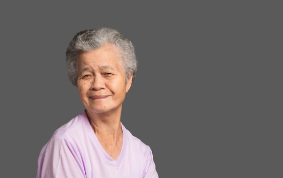 An elderly Asian woman looking at the camera with a smile while standing on a grey background in the studio. photo