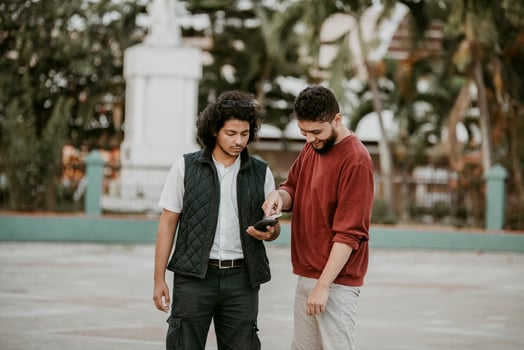 Portrait of two smiling guys using cell phone outdoors. Two happy friends using the mobile phone on the street photo