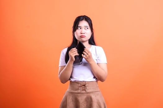 A Woman with an Empty Wallet Looks Up with Disappointment on Orange Background photo