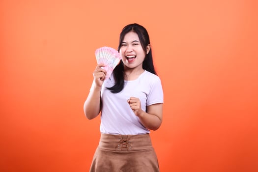 Excited woman holding a fan of money in front of an orange backdrop photo