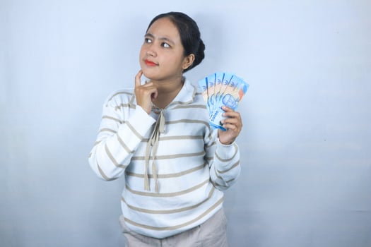 Beautiful asian woman in sweater thinking something while holding money isolated on white background photo