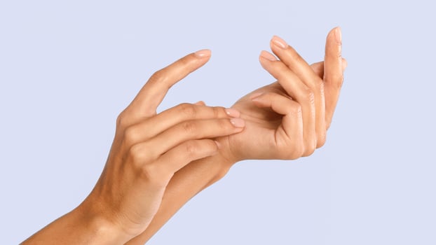Closeup cropped view of beautiful female hands with pink nude natural manicure, woman touching soft skin after spa treatment isolated on blue studio white background, applying cream. Skincare Concept photo