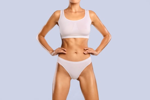 Closeup Cropped Frontal View Of Slim Lady With Perfect Body Shape And Flat Tummy Posing Holding Hands On Hips Isolated On Blue Studio Background, Woman Wearing White Lingerie. Fitness, Diet Concept photo