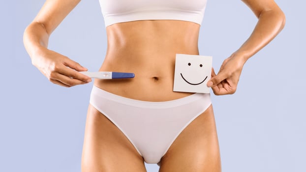 Positive Result. Young woman holding pregnancy test with two stripes and sticker post-it note card with smiley face. Unrecognizable female waiting for a long-awaited planned baby. Closeup cropped view photo