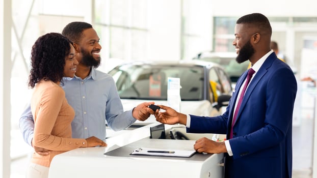 Car Sales. Handsome Black Manager Giving Key To Happy Couple In Dealership Center After Buying New Vehicle, Greeting African American Spouses With Successful Purchase In Automobile Showroom photo