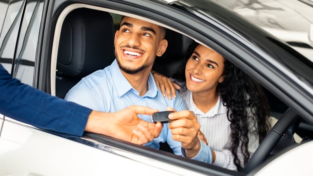 Happy middle-eastern couple buying car in huge showroom, taking automobile key from young handsome salesman while sitting inside auto. Cheerful arab man and woman purchasing beautiful vehicle, closeup photo
