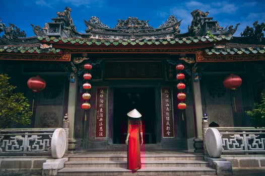A woman in a traditional Vietnamese costume, a conical hat with a fan in her hands against the background of an ancient building in Hoi An. photo