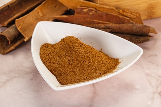 A bowl of cinnamon powder and sticks on a marble surface photo