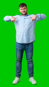 Man in a blue striped shirt and jeans gesturing downward against a bright green background photo