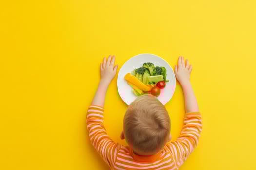 A young child reaches for a plate of fresh vegetables on a bright yellow table, promoting healthy eating habits at home photo