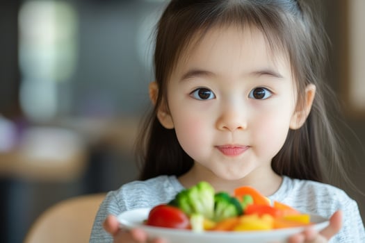 Young child happily holds a colorful plate of fresh vegetables and fruits in a bright indoor setting photo