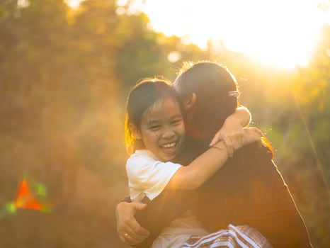 Mother and daughter are playing together in the park. Happy mother hugging her daughter sitting in the park with sunset light in nature. photo